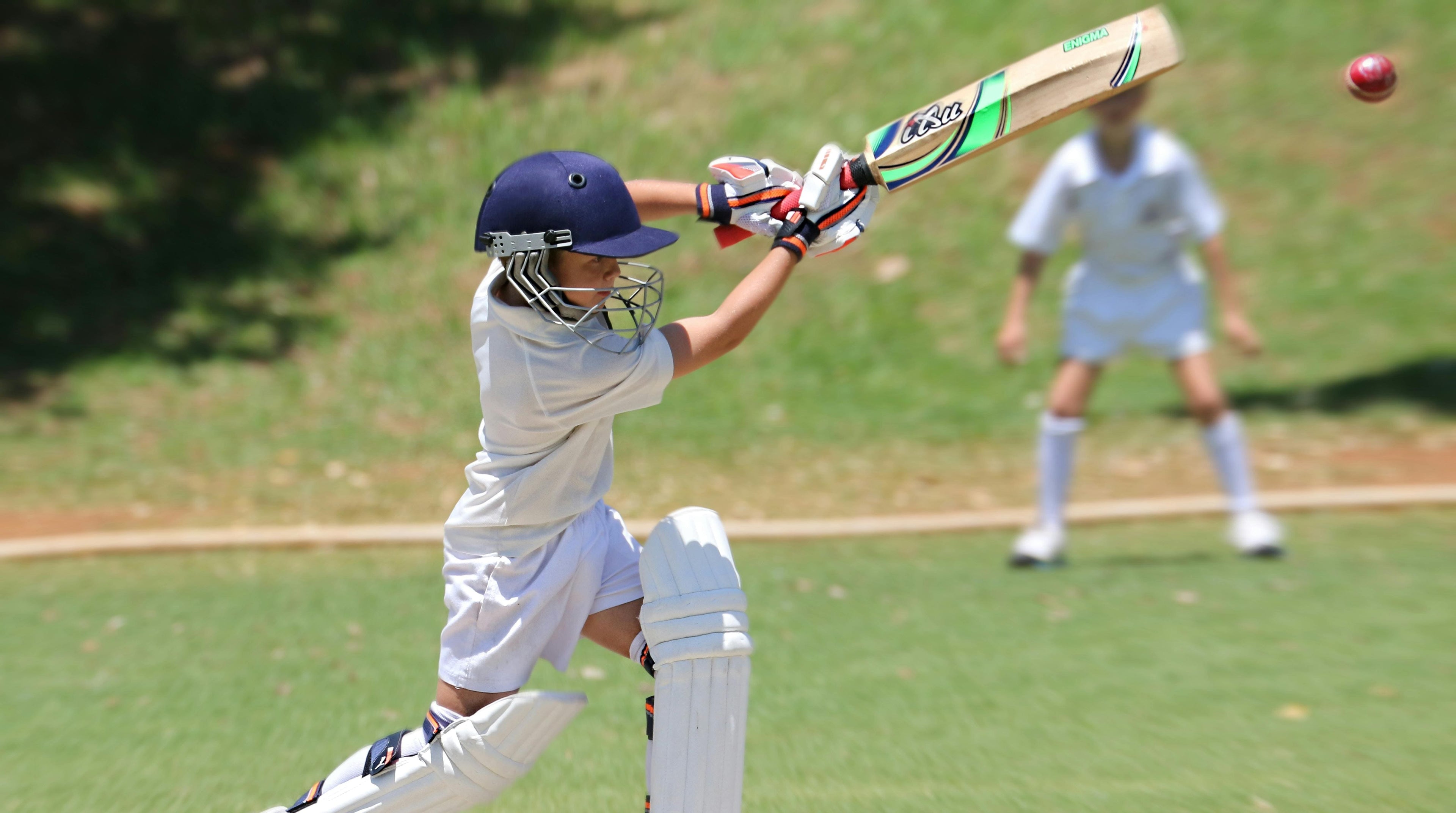 Junior cricketer in action on a cricket field with a ball and bat.