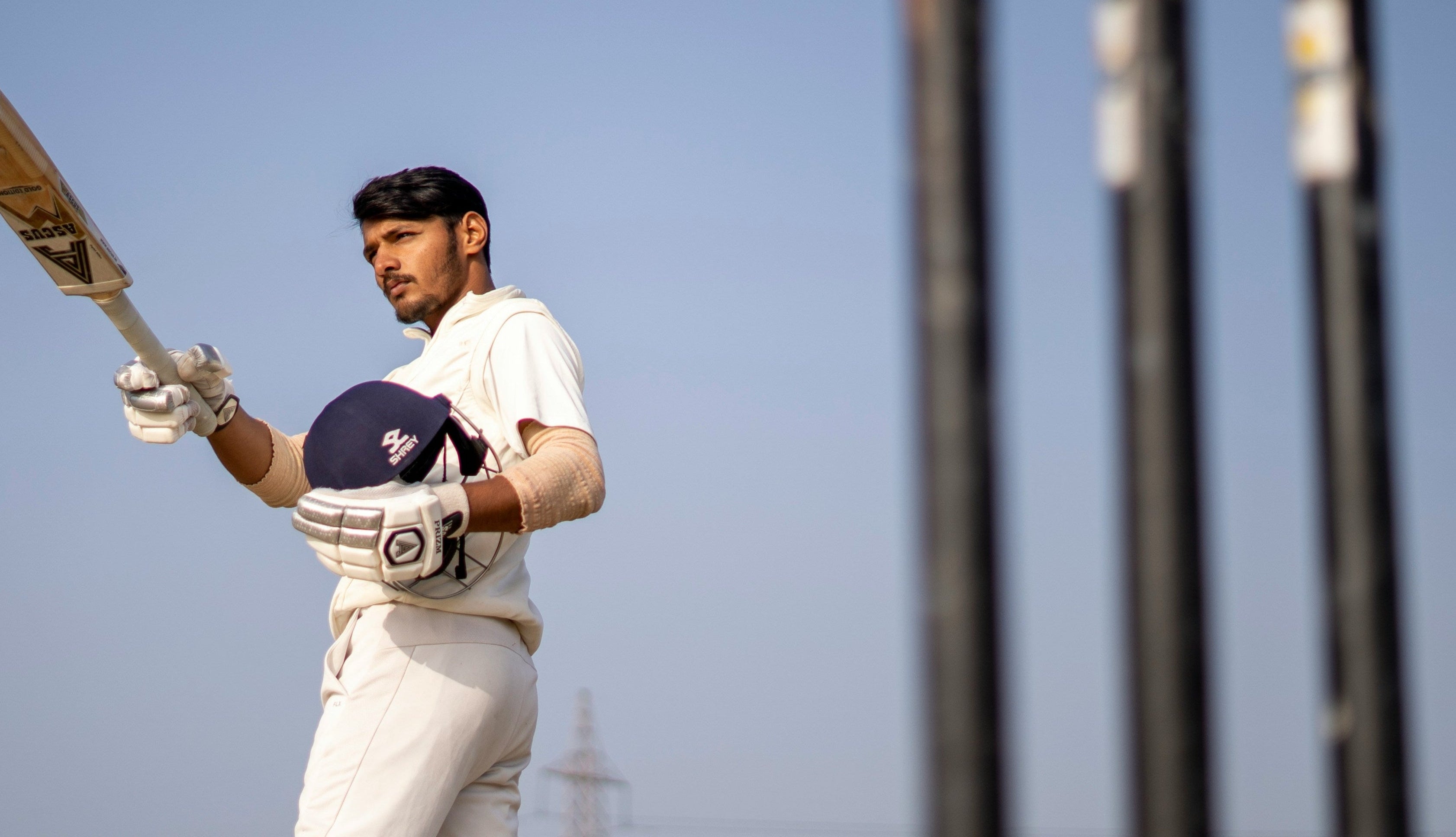 Cricketer holding a bat with clear blue sky and stumps in the background